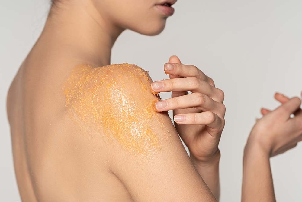 Woman using sugar body exfoliator on shoulder