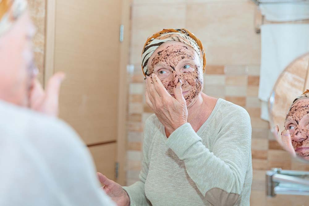 Senior woman applying facial exfoliator in mirror